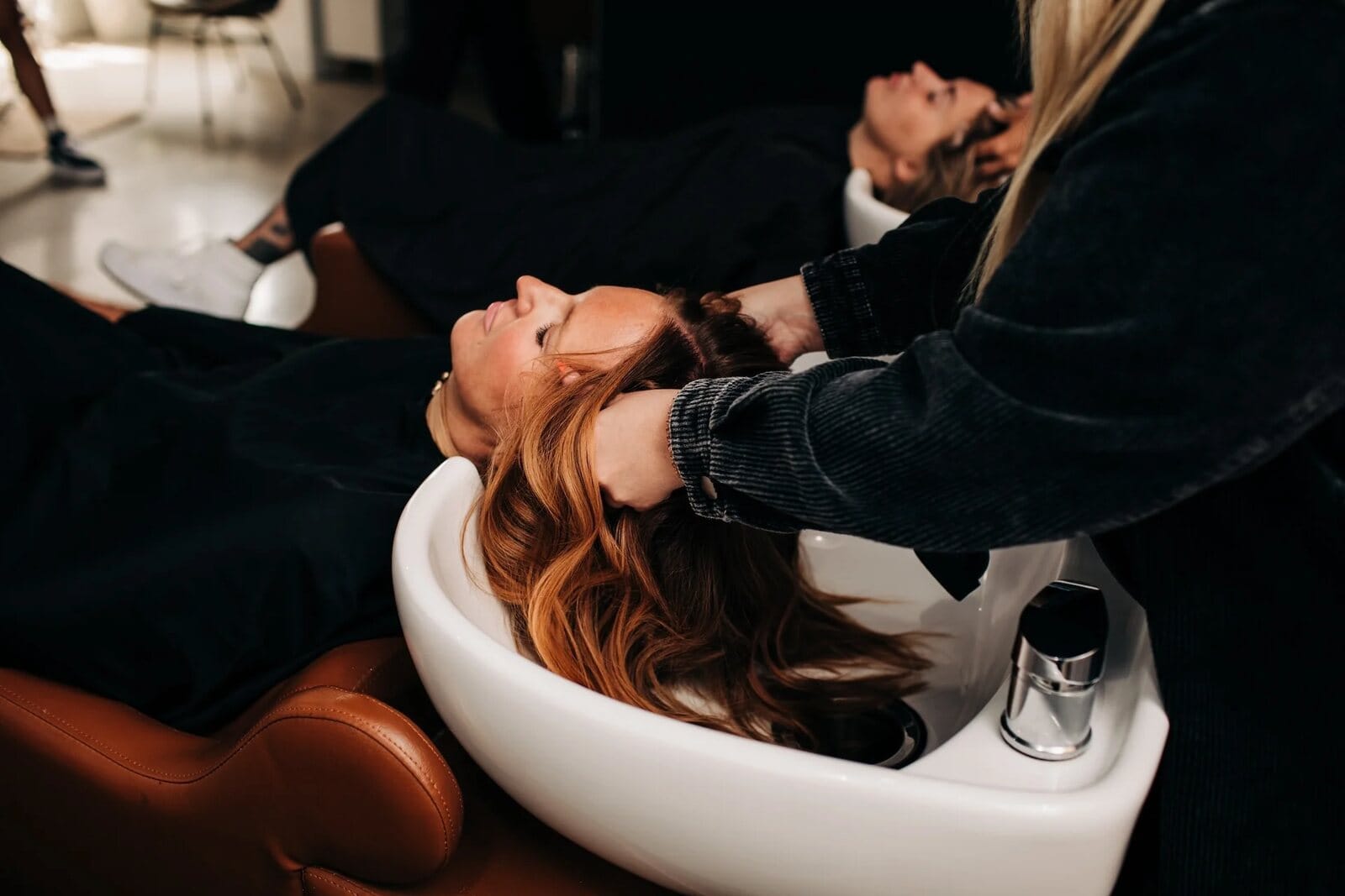 Guest with dimensional copper hair relaxing during a color service at Artistry Lounge Hair Studio in Bay City